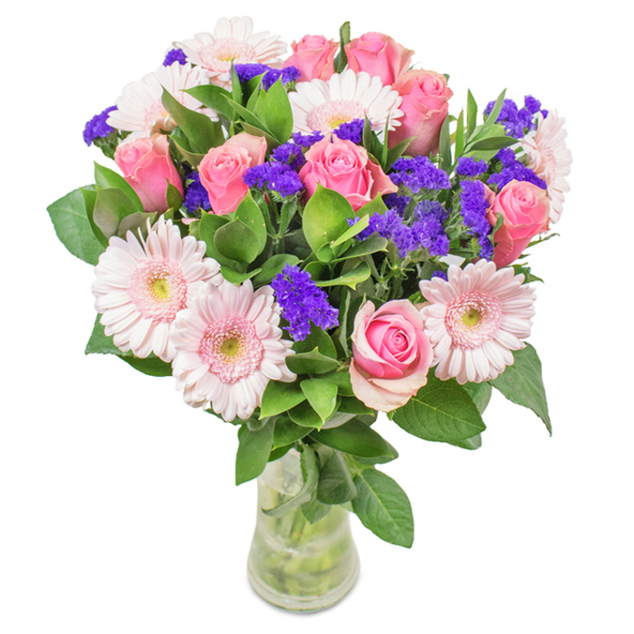 A vibrant, expertly arranged bouquet from Egham, gracefully displayed in a clear glass vase upon a crisp white surface. The focal point is a harmonious gathering of seven to nine pink roses, their petals at various stages-some tightly budded, others beginning to unfurl in perfect spirals-each one emblematic of classic romance and heartfelt intention. Bordering the roses sit five to seven pale pink gerbera daisies, their broad faces and multitude of petals like a radiant blush at sunset, easily recognized across Egham's charming riverside homes. The arrangement is elevated by clusters of lively purple statice, their smaller, textured blossoms injecting energy and refined contrast. Beneath, a bed of lush, deep green foliage adds refreshing vibrancy, conjuring the freshness of spring parks surrounding Egham. Visible stems in water retain a natural, fresh-from-the-florist appeal, making the bouquet ideal as a thoughtful birthday surprise, a graceful Mother's Day gift, or a welcoming touch for local offices and gatherings. This curated display embodies celebration, affection, and the spirit of Egham hospitality.